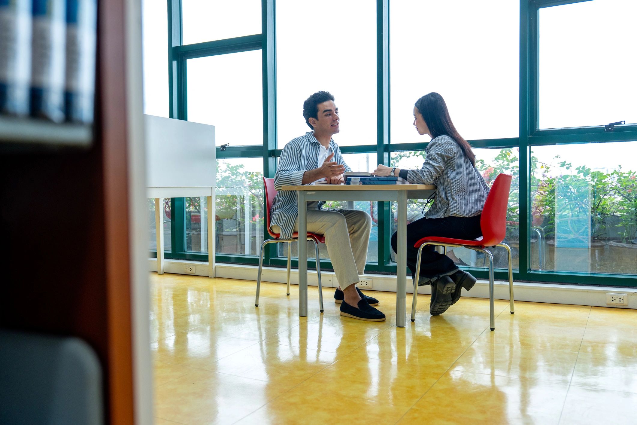 Two researchers discussing work at a table near a window